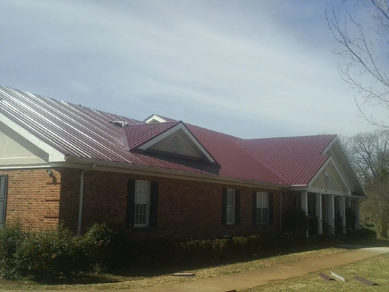 Red metal roof with gabled entries on a long brick building, from a Hail Damage Roof Repair job in Paskenta