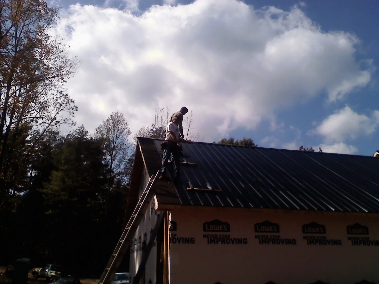 Roofer fastening dark metal panels high against a cloudy sky, from a Roof Inspection job in Paskenta